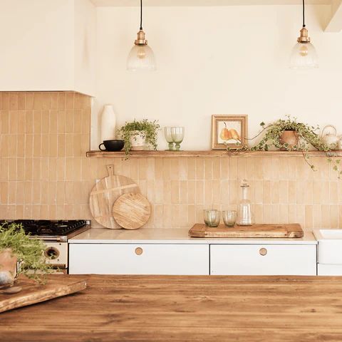 a modern white kitchen with sleek countertops, a terracotta tile backsplash, a shelf with decor and greenery