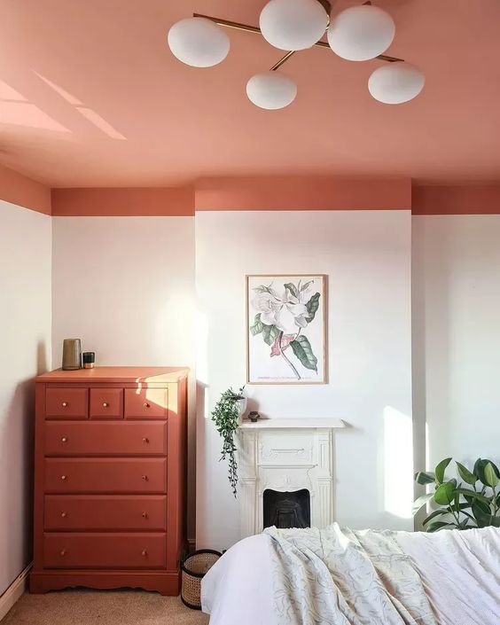 a neutral bedroom gone bright with a coral ceiling and a matching dresser, a small fireplace, a bed and some greenery