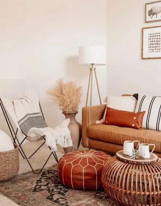 A neutral boho space with a tan leather sofa and a rust colored ottoman, striped textiles, pampas grass and a wooden table