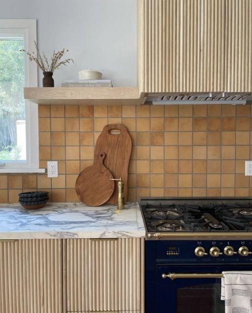a neutral fluted kitchen with white stone countertops and a terracotta tile backsplash, open shelves and brass touches