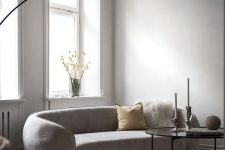 a neutral minimalist living room with a curved sofa, a pendant lamp, a coffee table, pillows and blooms in a vase