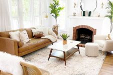 a neutral modern living room with a fireplace, a tan leather sofa, neutral chairs, a coffee table, potted greenery and lamps