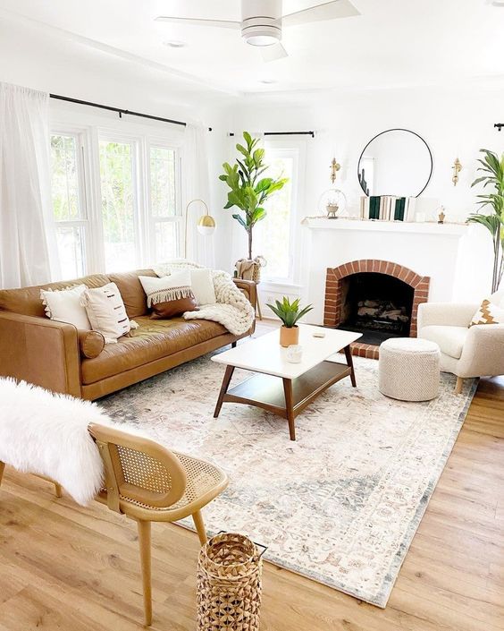 a neutral modern living room with a fireplace, a tan leather sofa, neutral chairs, a coffee table, potted greenery and lamps