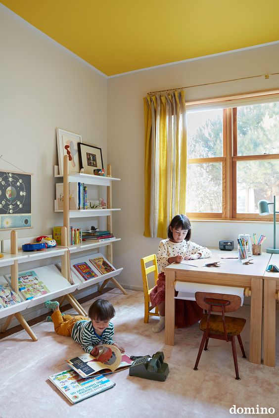 a playroom done with a yellow ceiling, a planked desk and open shelves, a large rug and yellow striped curtains