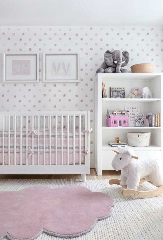 a pretty contemporary nursery with a pink spot accent wall, a white crib and a storage unit, layered rugs, pink bedding and lovely toys