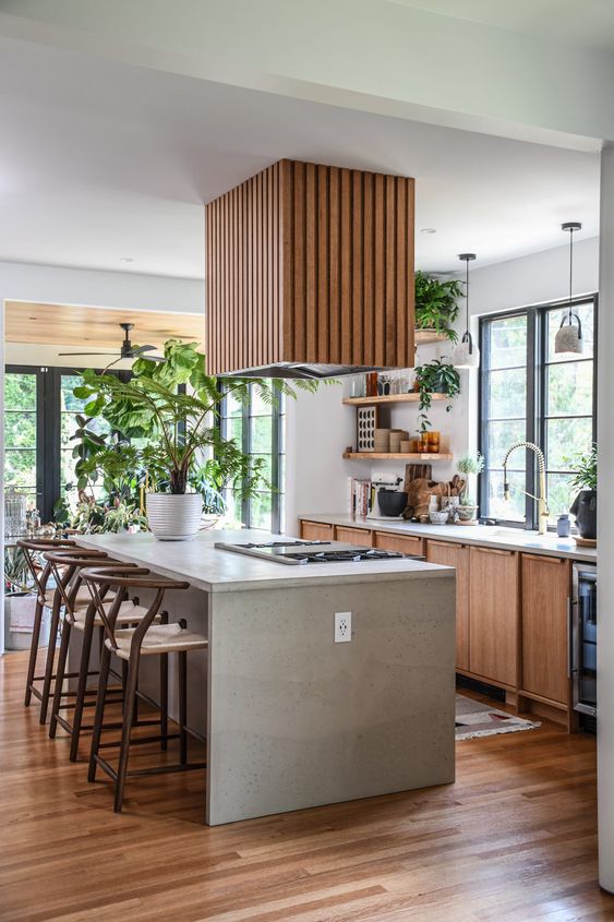 a pretty kitchen with stained cabinets, a white kitchen island with countertops, open shelves and a fluted hood plus a lot of greenery
