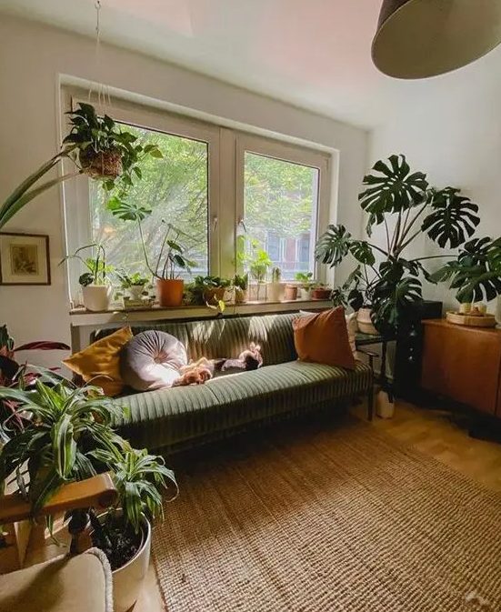 A pretty mid century modern living room with a green sofa and pillows, stained furniture, a rug, lots of potted plats