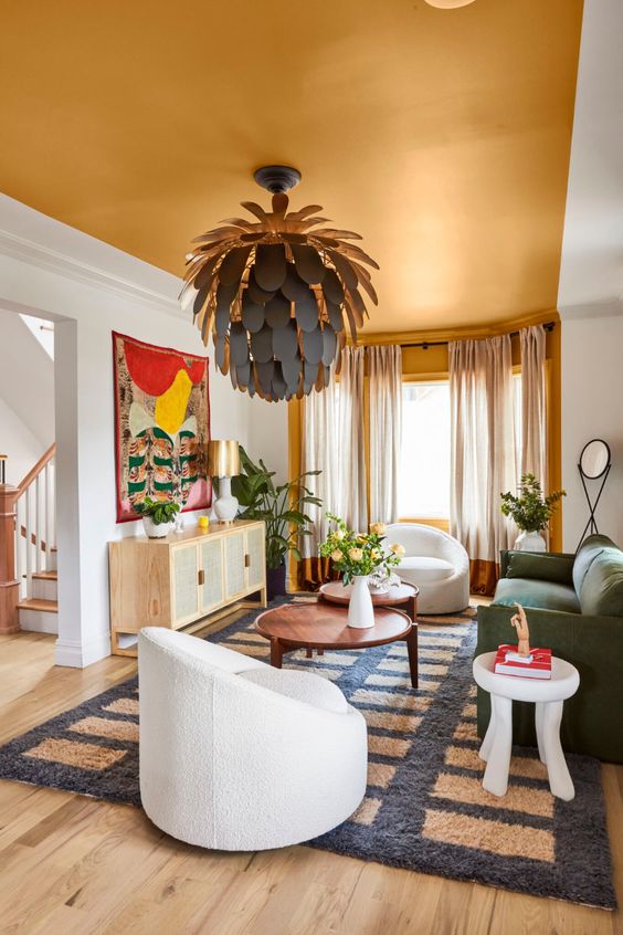 a refined and bold living room with a gold ceiling, a green sofa, white chairs, a cane sideboard and a unique petal chandelier