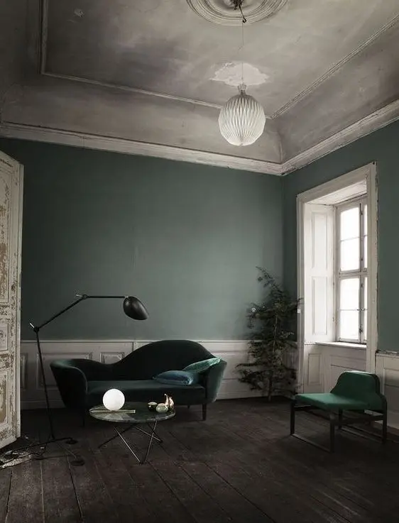 a refined living room with grey green walls, hunter green velvet furniture, white paneling and a chic ceiling