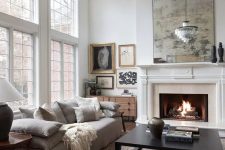 a refined neutral living room with a low grey sofa with lots of pillows, a low coffee table, a fireplace, a crystal chandelier and a gallery wall