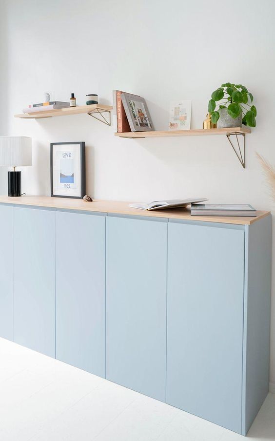 a serene light blue sideboard made of an IKEA Metod cabinet, with a wooden countertop, with books and decor and some shelves over
