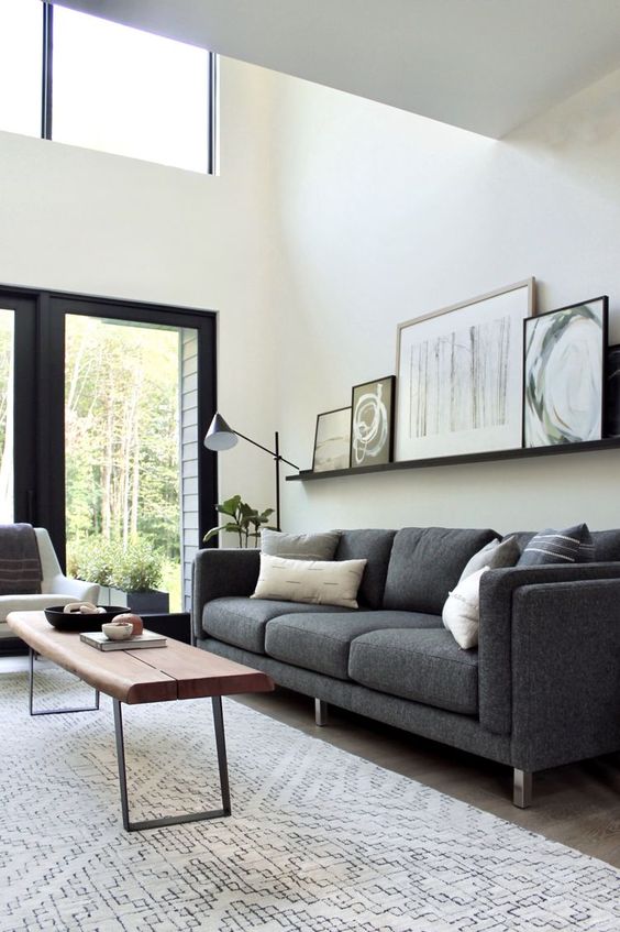 a serene living room with a grey sofa and pillows, a creamy chair, a coffee table bench, a ledge gallery wall and some lamps