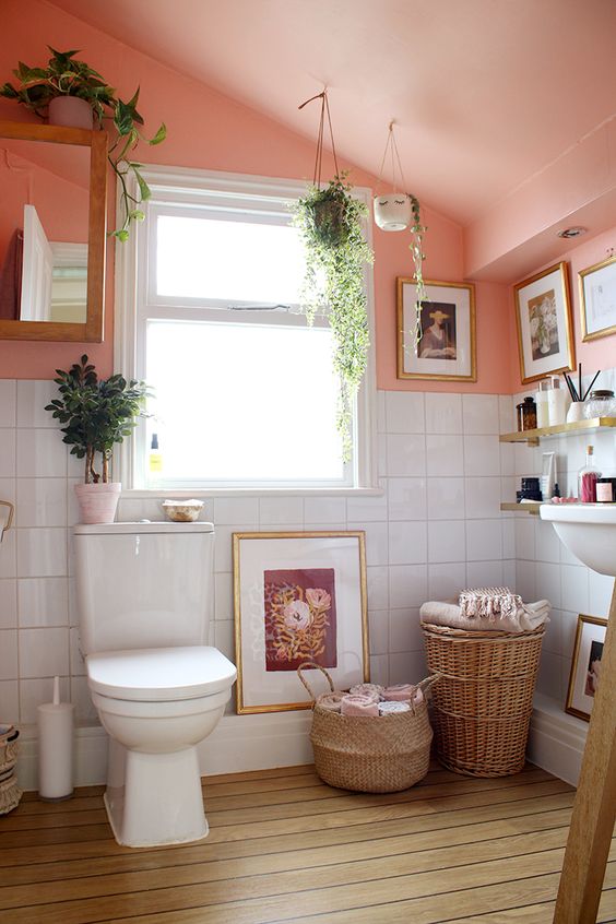 a small and cozy bathroom done with a pink sloped ceiling,a sink, a toilet, some baskets and potted plants plus decor