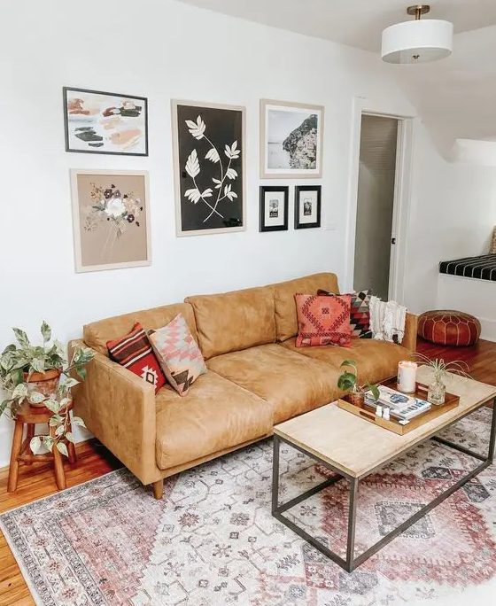 a small boho living room with a tan leather sofa, a coffee table, a gallery wall, a boho printed rug and greenery