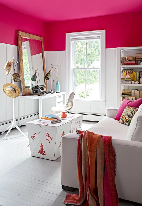 a small space done cool with a fuchsia ceiling, a desk, a chair, a white sofa and colorful pillows plus a shelving unit