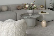 a sophisticated airy living room with a dove grey sofa, a white boucle chair, coffee tables and gold table and floor lamps