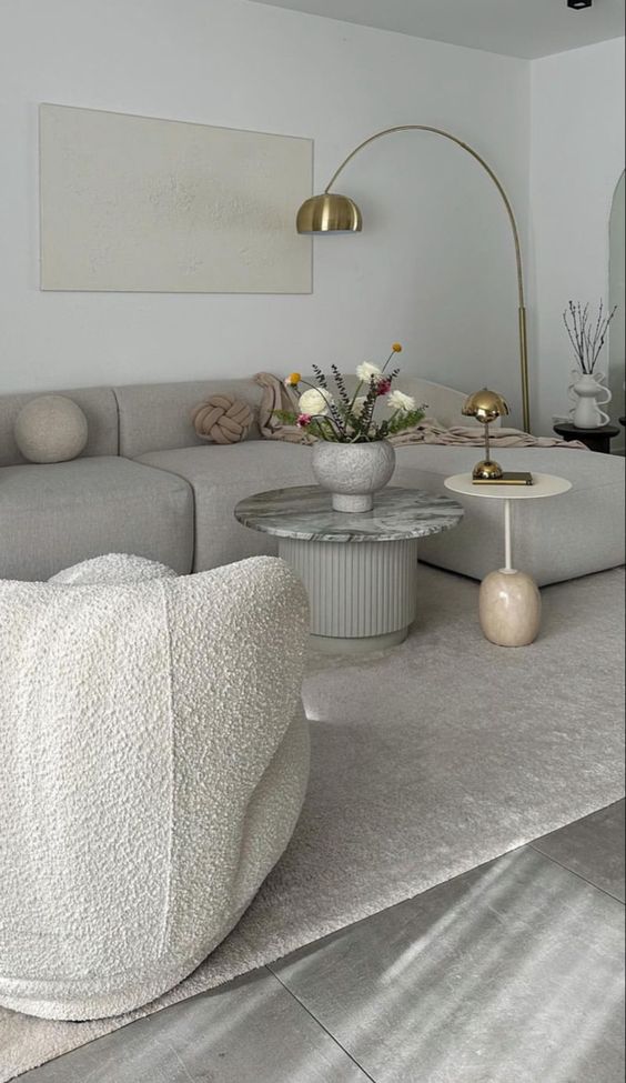 a sophisticated airy living room with a dove grey sofa, a white boucle chair, coffee tables and gold table and floor lamps