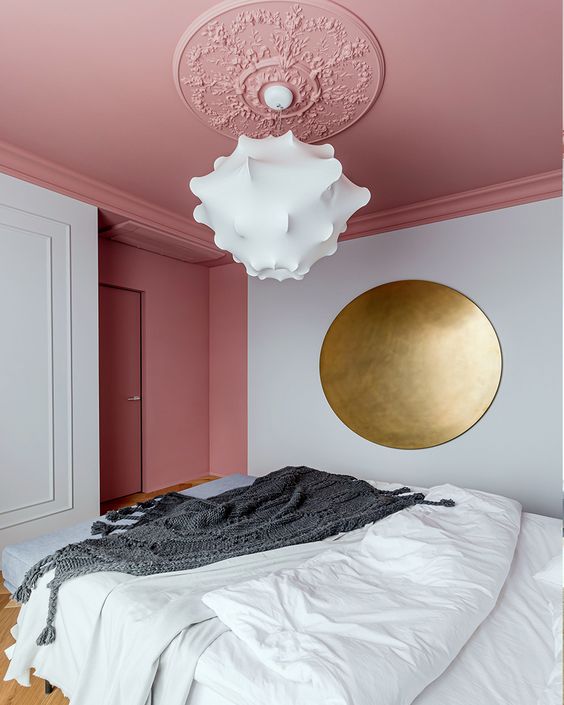 a sophisticated bedroom with a pink ceiling, a bed with neutral bedding, a large brass circle as art and a gorgeous cloud chandelier