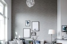 a stylish Scandinavian living room with a grey accent wall, a grey sectional with pillows, coffee tables and a pendant lamp