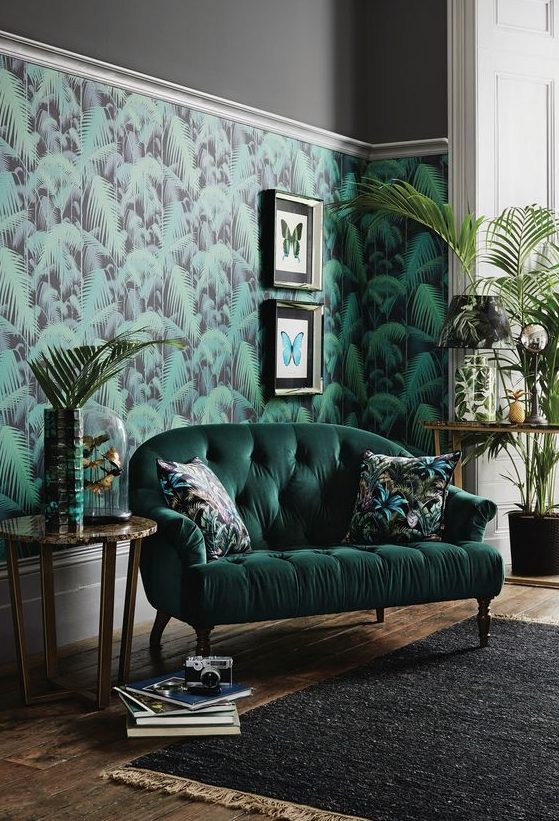 a stylish living room with a tropical leaf wall, a hunter green sofa, potted greenery and artworks