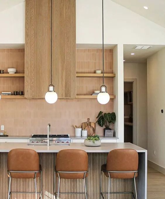 A warm colored kitchen with a terracotta tile wall, a fluted hood, open shelves, a fluted kitchen island and leather stools