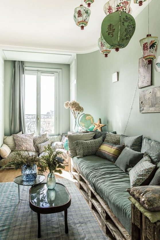 a welcoming green living room with light green walls, curtains, a hunter green sofa and pillows, a printed rug and pendant lamps
