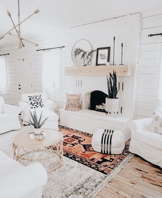 a white farmhouse living room with a fireplace, white seating furniture, a coffee table and some decor and layered rugs