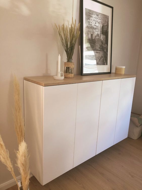 a white floating credenza of IKEA Metod with a butcherblock countertop, an artwork, a candle and decor
