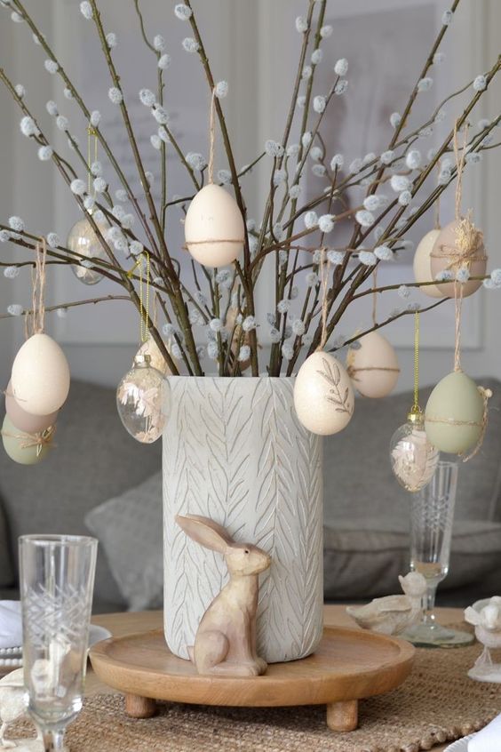 an Easter centerpiece of willow and plastic eggs decorated with neutral colors and clear palstic eggs with decor