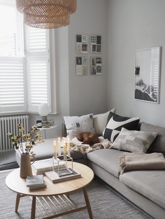 an airy Scandinavian space with a grey sectional sofa, a coffee table, printed pillows, a gallery wall and a woven pendant lamp