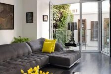 an airy living room with a graphite grey sectional, mirror coffee tables, touches of bold yellow and a glazed wall