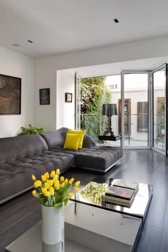 an airy living room with a graphite grey sectional, mirror coffee tables, touches of bold yellow and a glazed wall