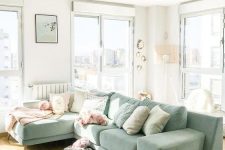 an airy living room with a light green sectional and neutral pillows, a rug and some greenery wreaths
