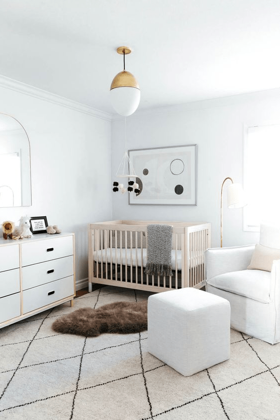 An airy modern nursery with white walls, white furniture and a light stained crib, layered rugs and abstract decor