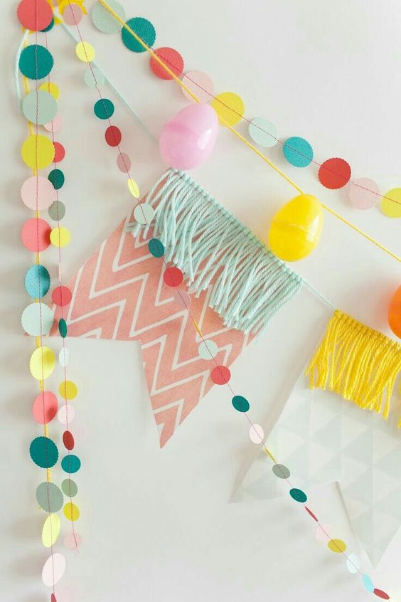 an arrangement of bright garlands, colorful paper ones, a colorful banner with fringe and a colorful plastic egg garland