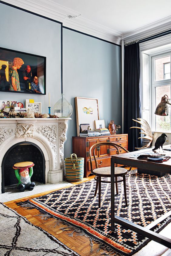 an eclectic home office with a fireplace, layered rugs, a vintage sideboard, chic decor and a desk