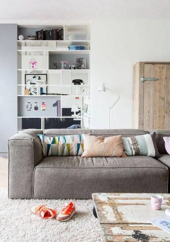 an eclectic living room with a rough wood storage cabinet, a grey low sofa, a shabby chic coffee table and a built-in shelving unit