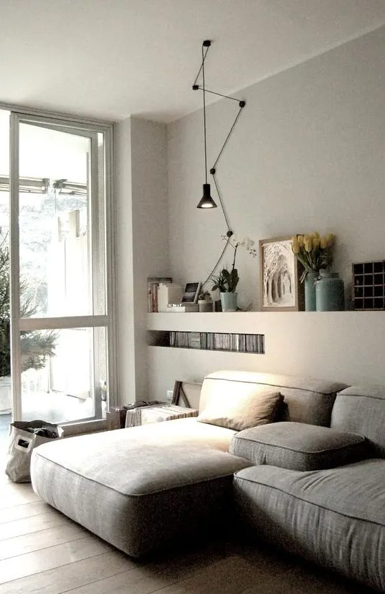 An ethereal Scandi living room with a low grey sectional, built in shelves, a black pendant lamp and some books