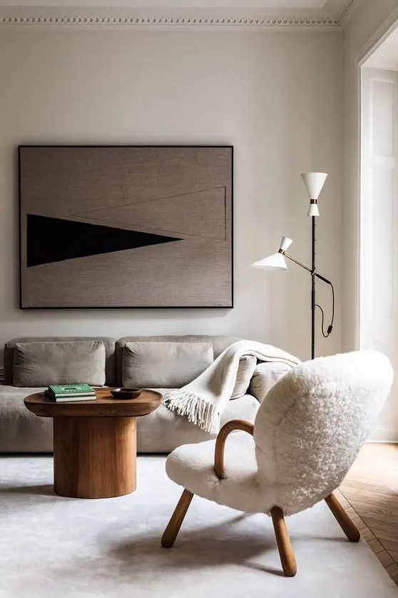 an ethereal Scandinavian living room with a grey low sofa, a creamy chair, a wooden coffee table, a floor lamp and a bold artwork