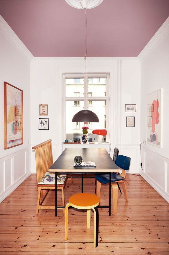 an exquisite dining room with a lilac ceiling, a black table and mismatching chairs, some cool artwork