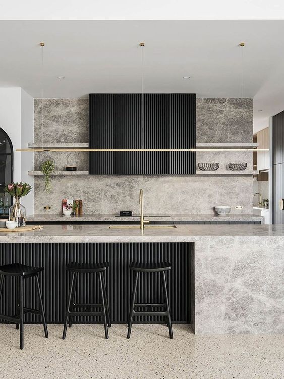 an exquisite kitchen with black cabinets, a grey backsplash and countertops, a fluted kitchen island and a hood, black stools