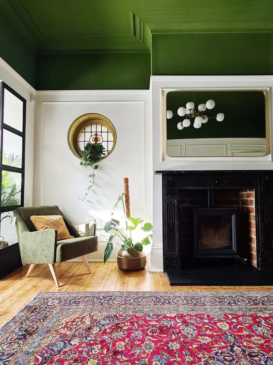 An eye catchy living room with a green ceiling, a hearth, a green chair, a round window, a bold printed rug and a potted plant
