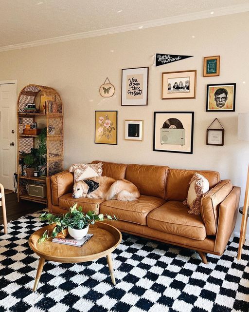 An eye catchy living room with a tan leather couch, a checked rug, a gallery wall, a shelving unit and a coffee table