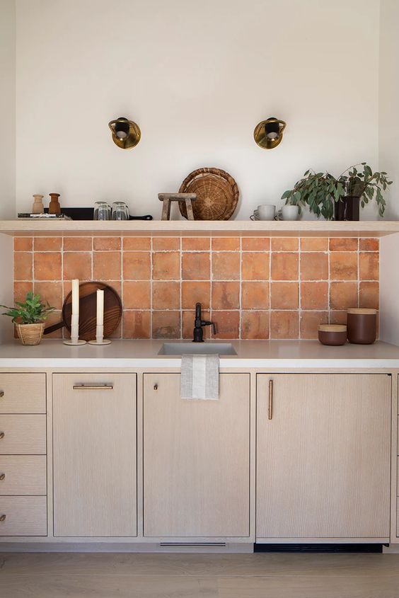 light-stained kitchen cabinets, a terracotta tile backsplash, an open shelf with decor and white countertops