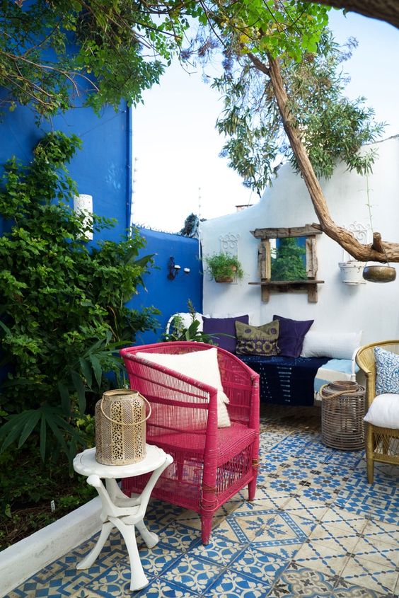 a Mediterranean terrace clad with blue tiles, a fuchsia chair, a navy sofa with pillows, greenery and a tree