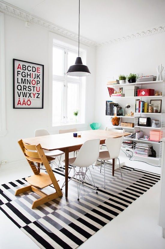 a Scandinavian dining room with a shelving unit, a striped rug, a table and mismatching chairs, an artwork and a pendant lamp