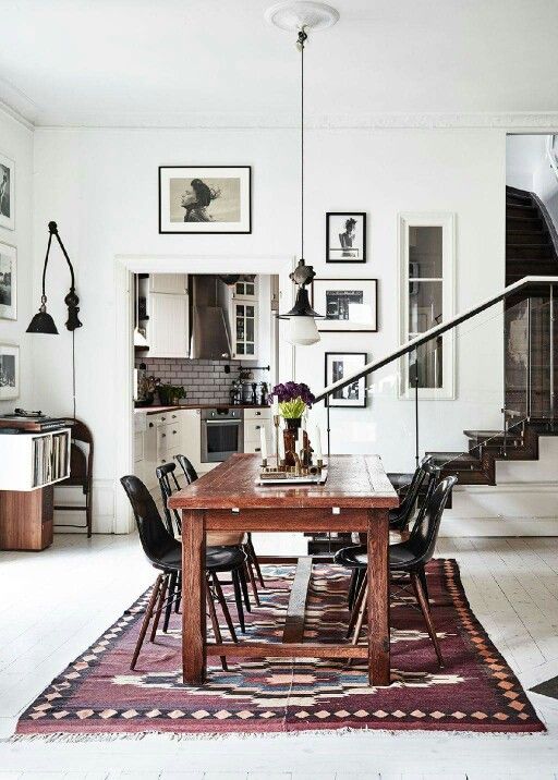 a Scandinavian dining room with a stained table and black chairs, a printed boho rug, some lamps and a black and white gallery wall