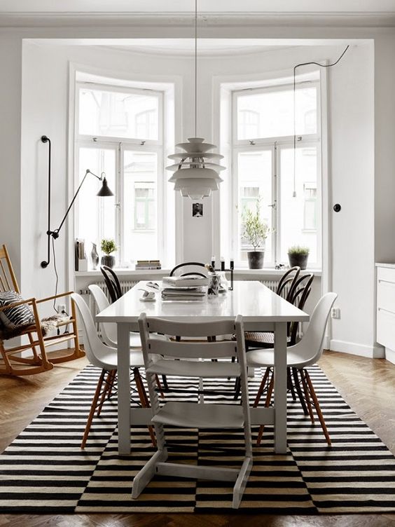 a Scandinavian dining room with a white table and black and white chairs, a striped rug, a pendant lamp and a rocker chair