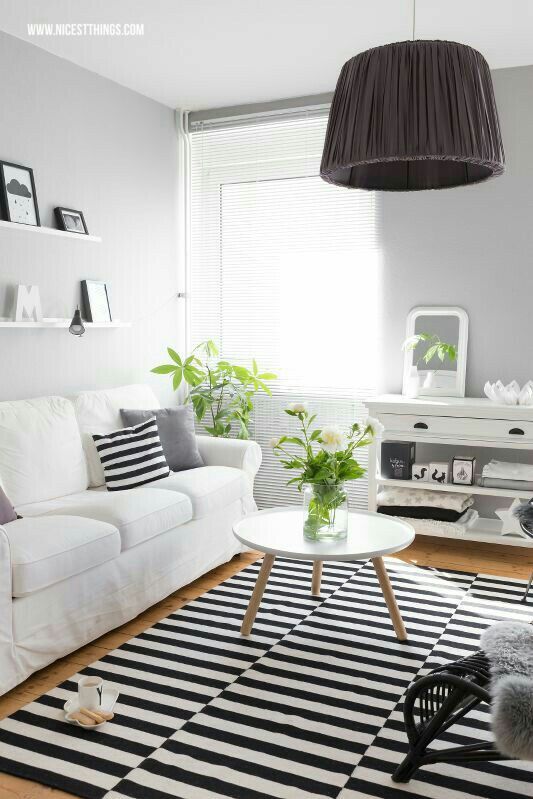 a Scandinavian living room with a white sofa and console, a coffee table, ledges with decor, a stripe rug and some greenery and blooms