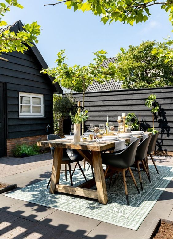 a Scandinavian terrace with a black fence, a stained table and black chairs, some greenery and candles is wow
